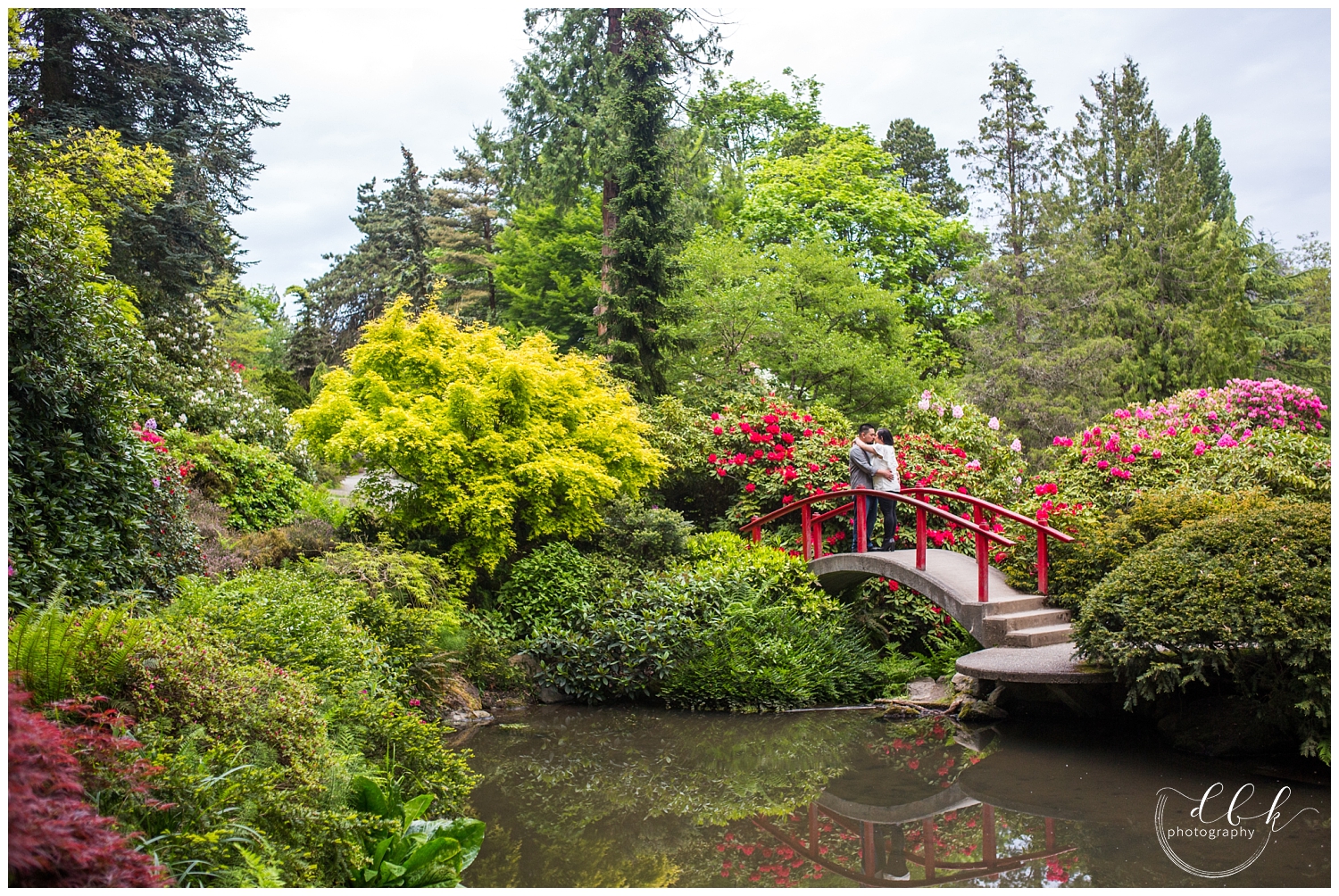 wide angle shot of couple kissing on red bridge in Japanese garden at Kubota Garden in Seattle