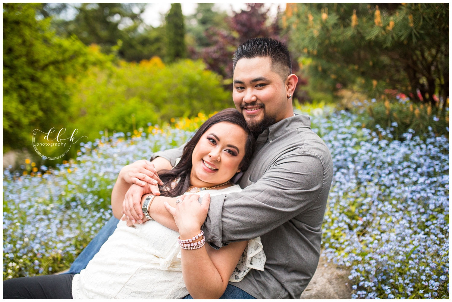man with his arms around his fiance in field of blue flowers at Kubota Garden in Seattle