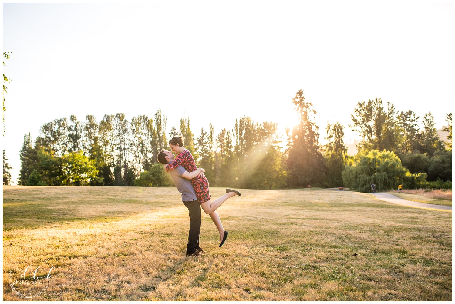 man lifting his future wife for a kiss in a field at Juanita Bay Park in Kirkland