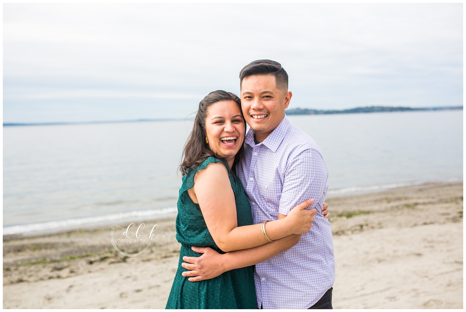 couple laughing at the camera during engagement portraits at Alki Beach in West Seattle