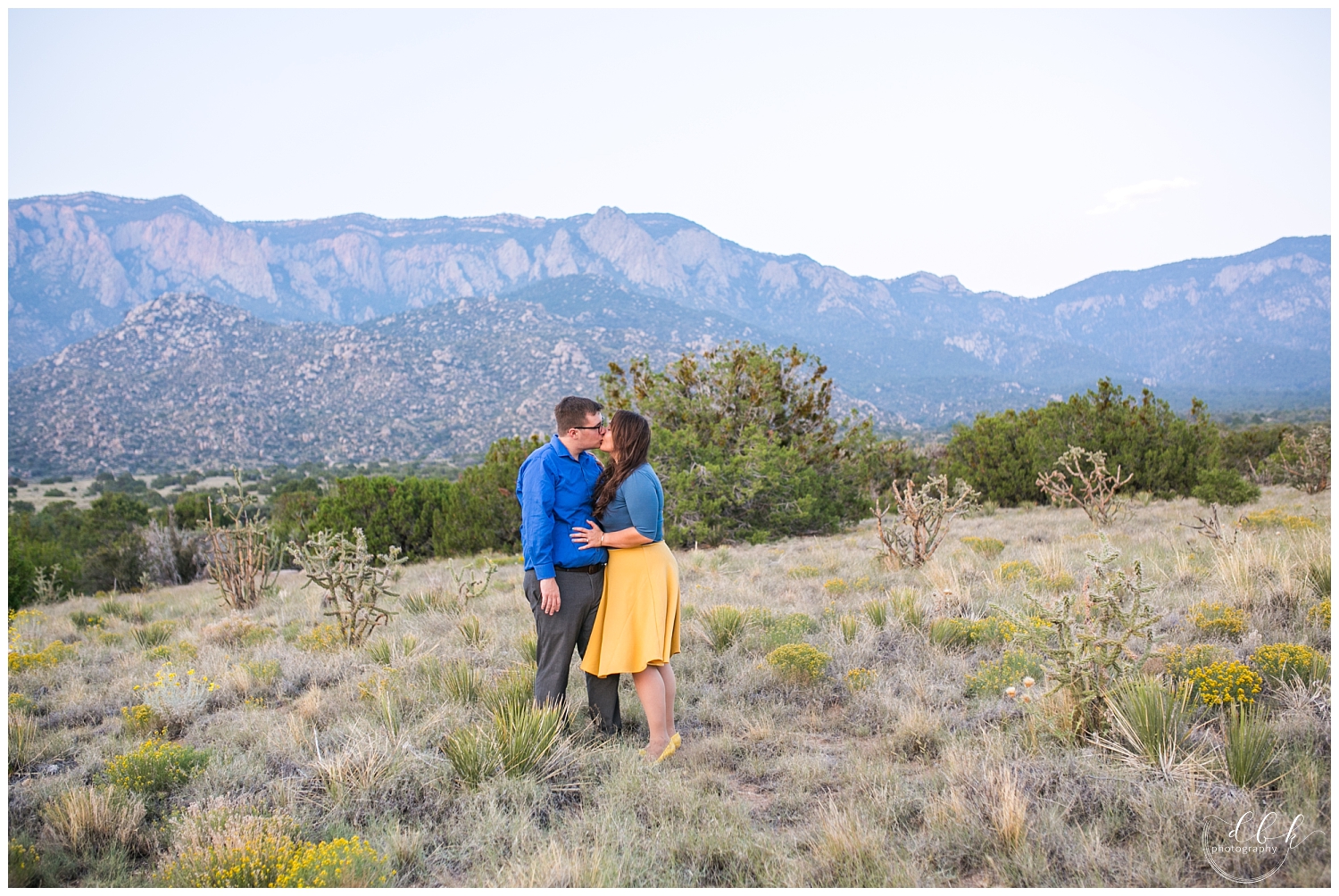 bride in yellow skirt kissing future groom in front of Sandia mountains 