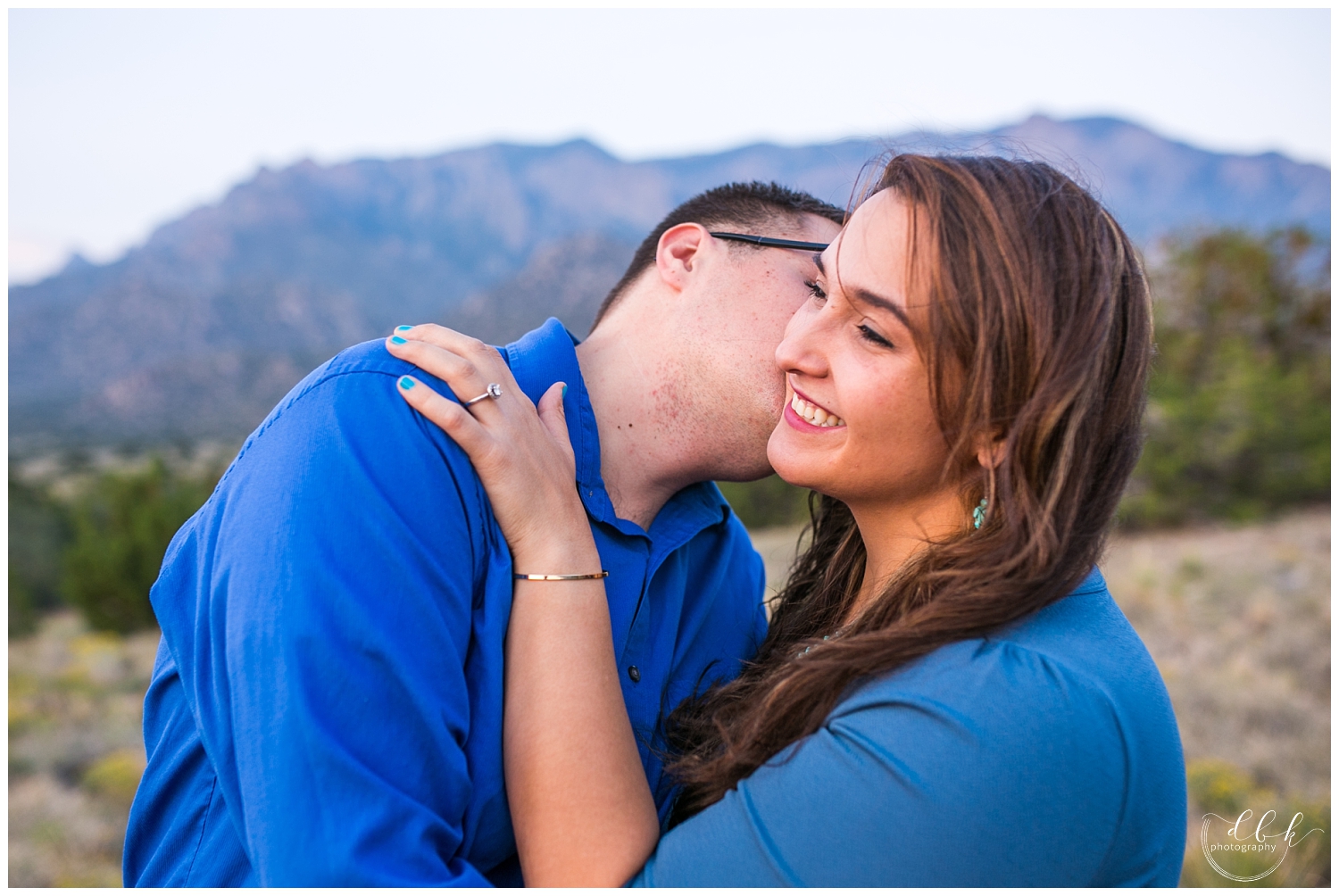 groom kissing bride on the cheek for engagement pictures by Sandia mountains in Albuquerque, New Mexico