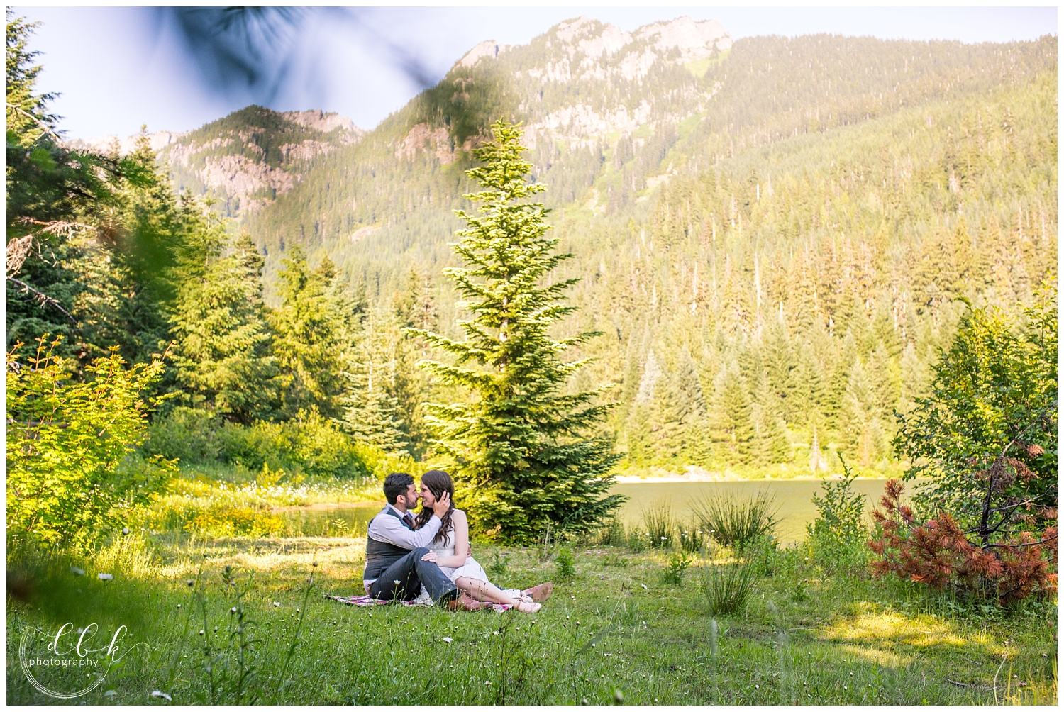 couple sitting in the grass by the water and mountains at Gold Creek Pond in Washington