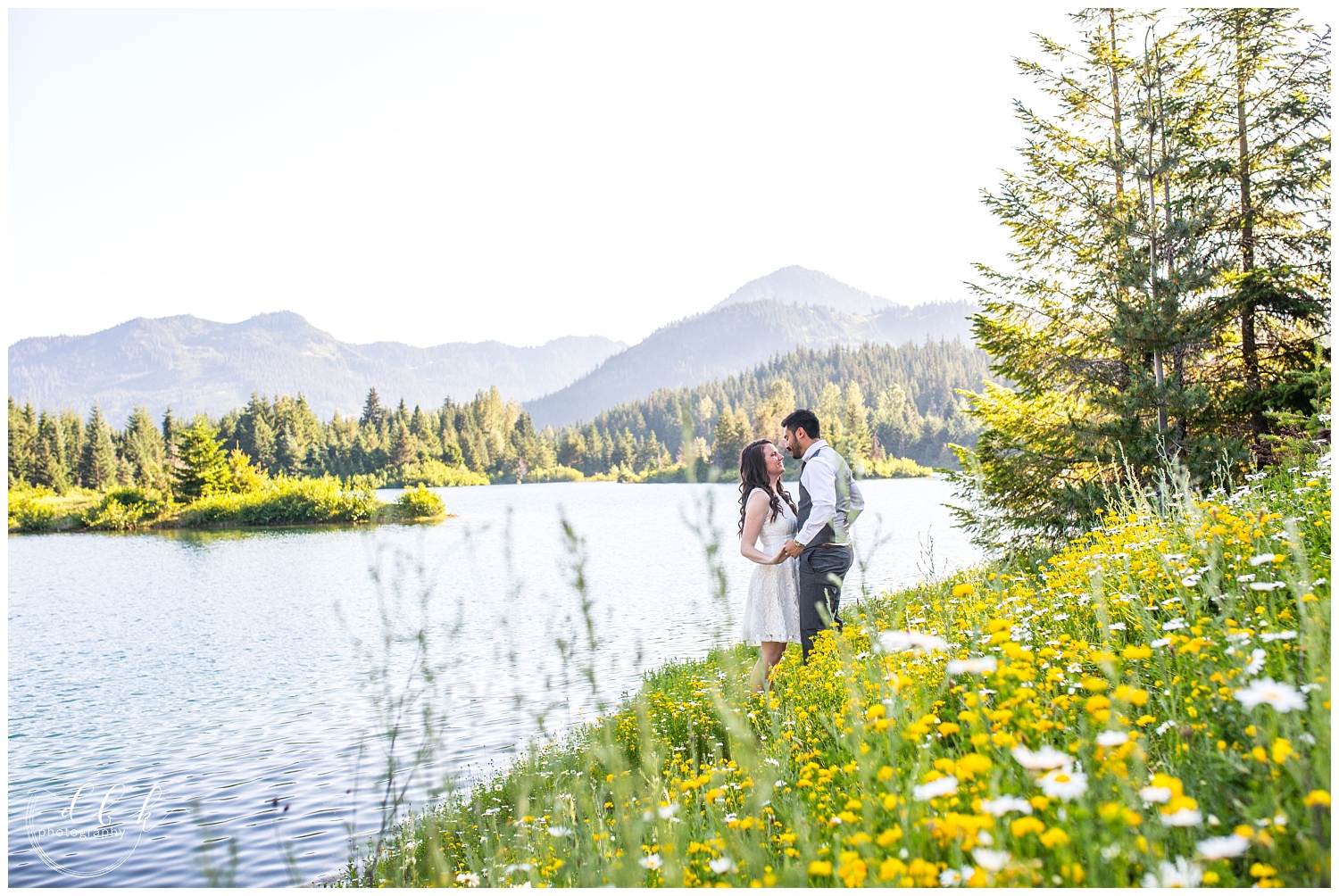 wide shot of wedding couple kissing on a hill of wildflowers over the water at Gold Creek Pond