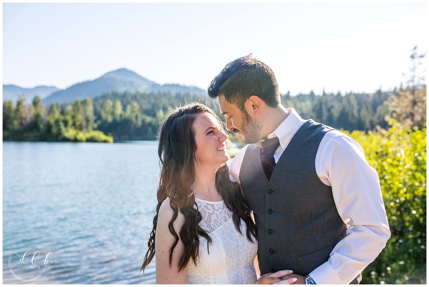 wedding couple touching noses by the water at Gold Creek Pond during summer engagement pictures