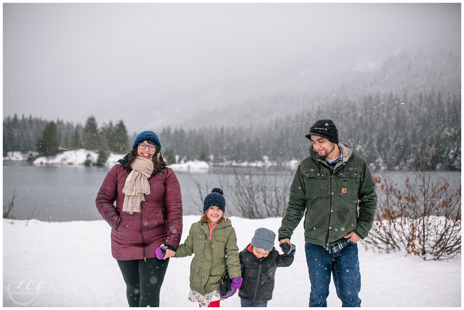 family of four bundled in coats walking toward the camera in the snow at Gold Creek Pond family portrait session