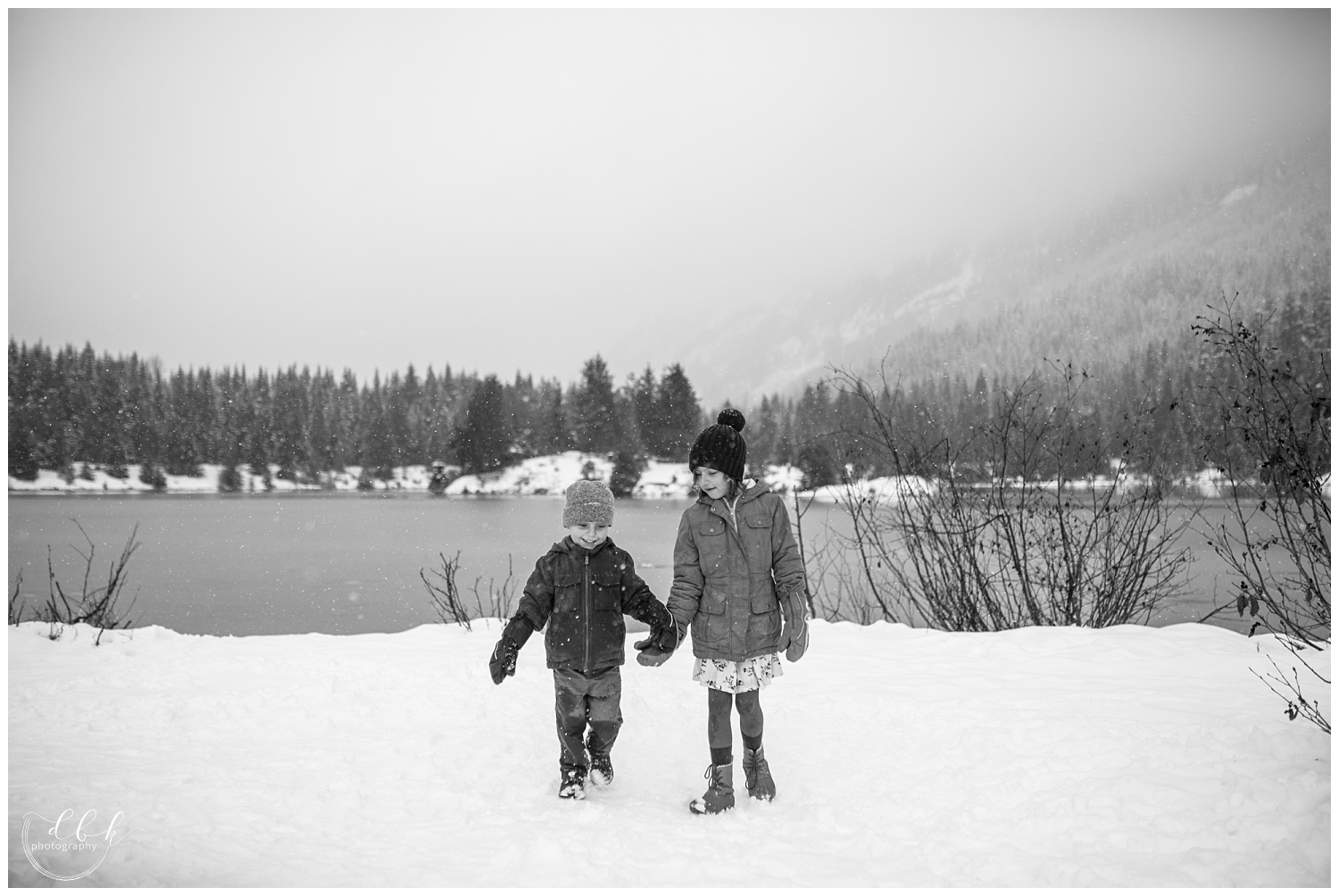 brother and sister holding hands walking toward the camera in the snow at Gold Creek Pond family portrait session