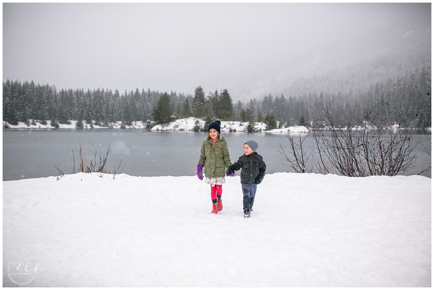 black and white shot of brother and sister holding hands walking toward the camera in the snow at Gold Creek Pond family portrait session