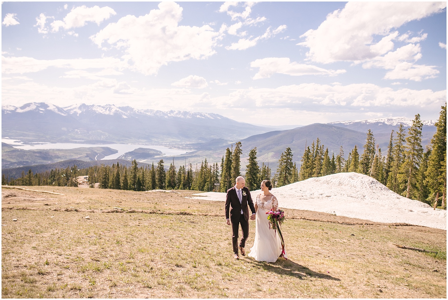 Bride and groom walking in front of sweeping mountain views at the summit of Keystone Colorado