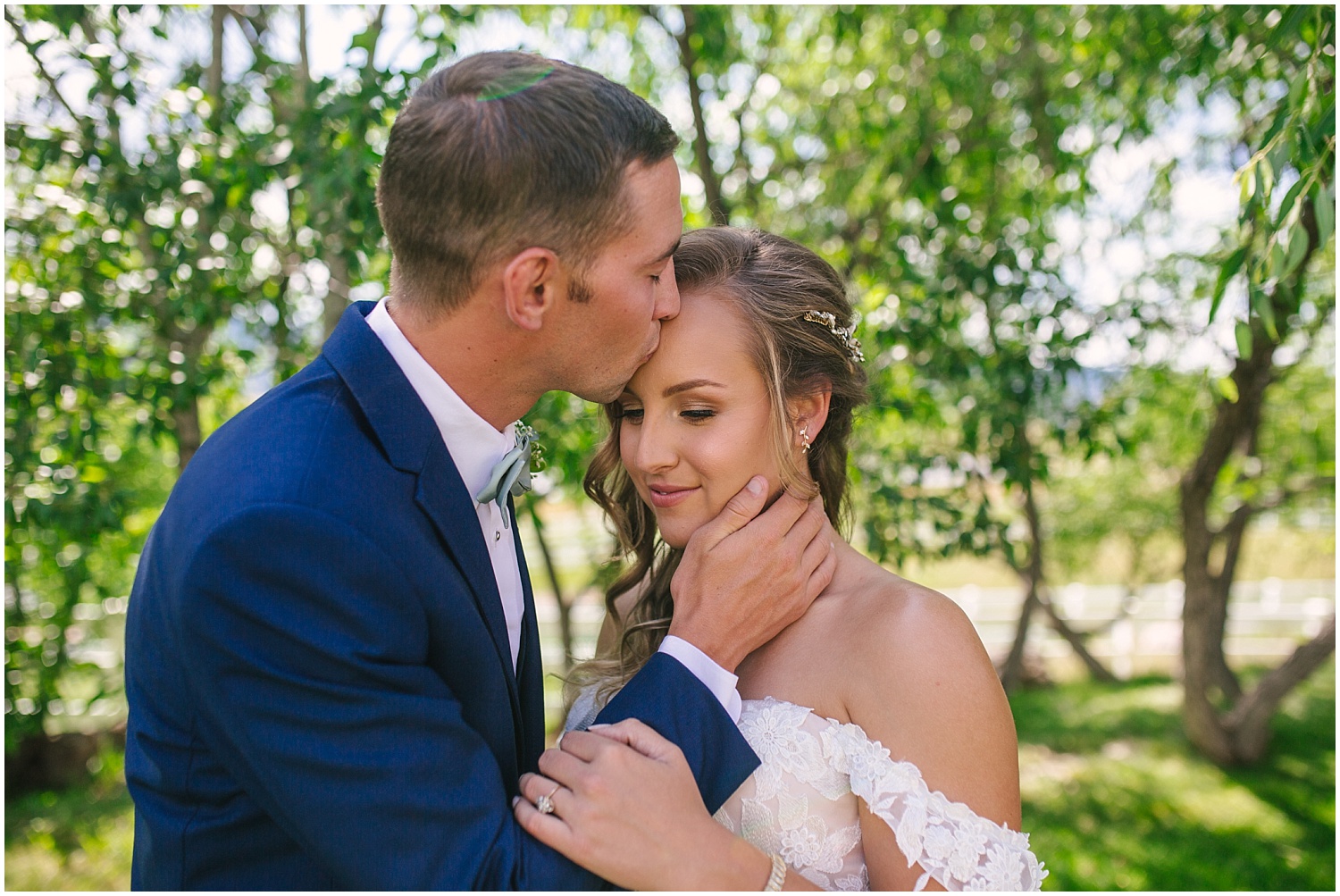 Groom in navy suit kisses his bride on the forehead at Crooked Willow Farms wedding