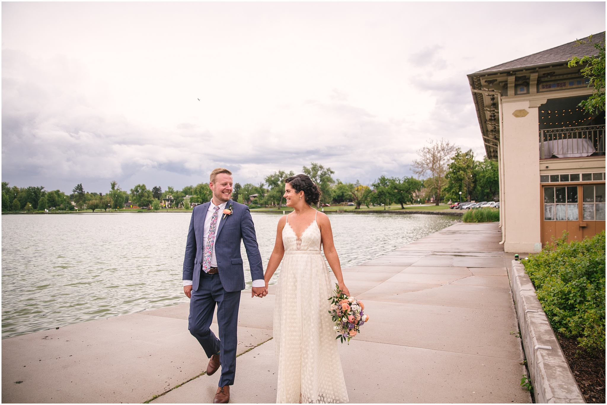 Bride and groom walking beside Smith Lake on a cloudy day in Washington Park in Denver Colorado