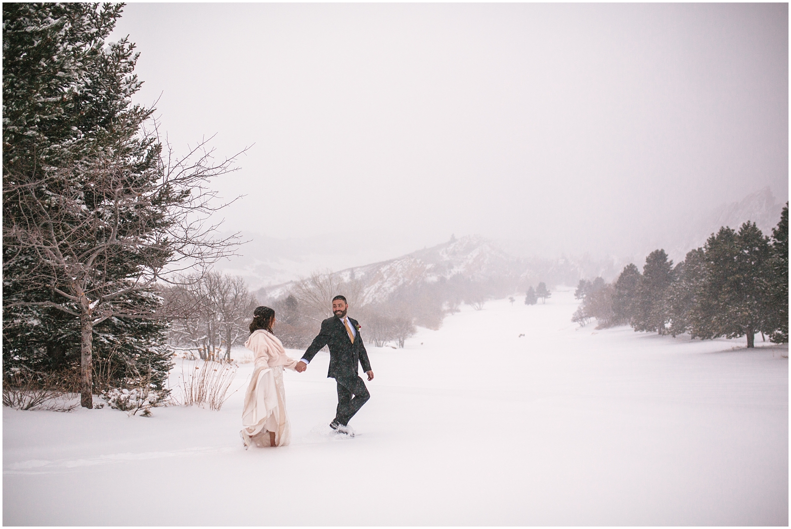 Bride and groom walking in the snow in front of red rocks at winter wedding at Arrowhead Golf Club