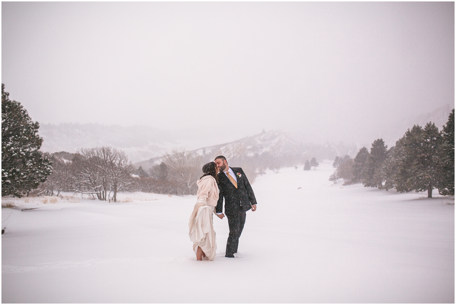 Bride and groom kissing in the snow in front of red rocks at winter wedding at Arrowhead Golf Club