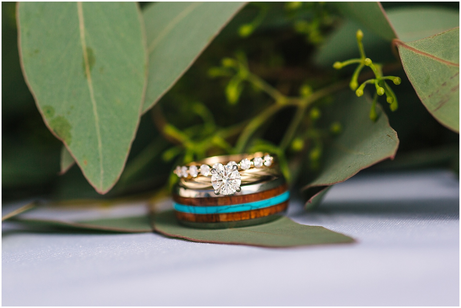 Turquoise, wood, and gold wedding bands sitting in eucalyptus 