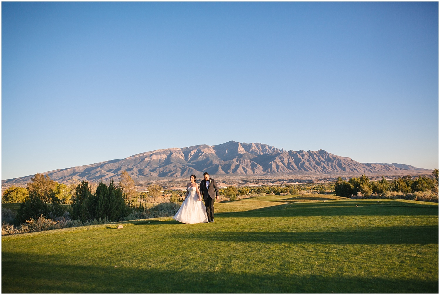Bride and groom walking in front of the Sandia Mountains on the Santa Ana Golf Course at Prairie Star Restaurant wedding