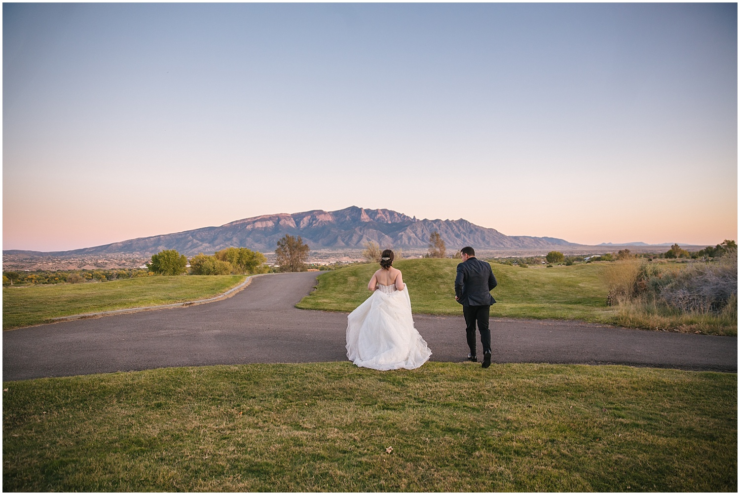 Bride and groom run towards the Sandia Mountains at sunset at Prairie Star Restaurant wedding