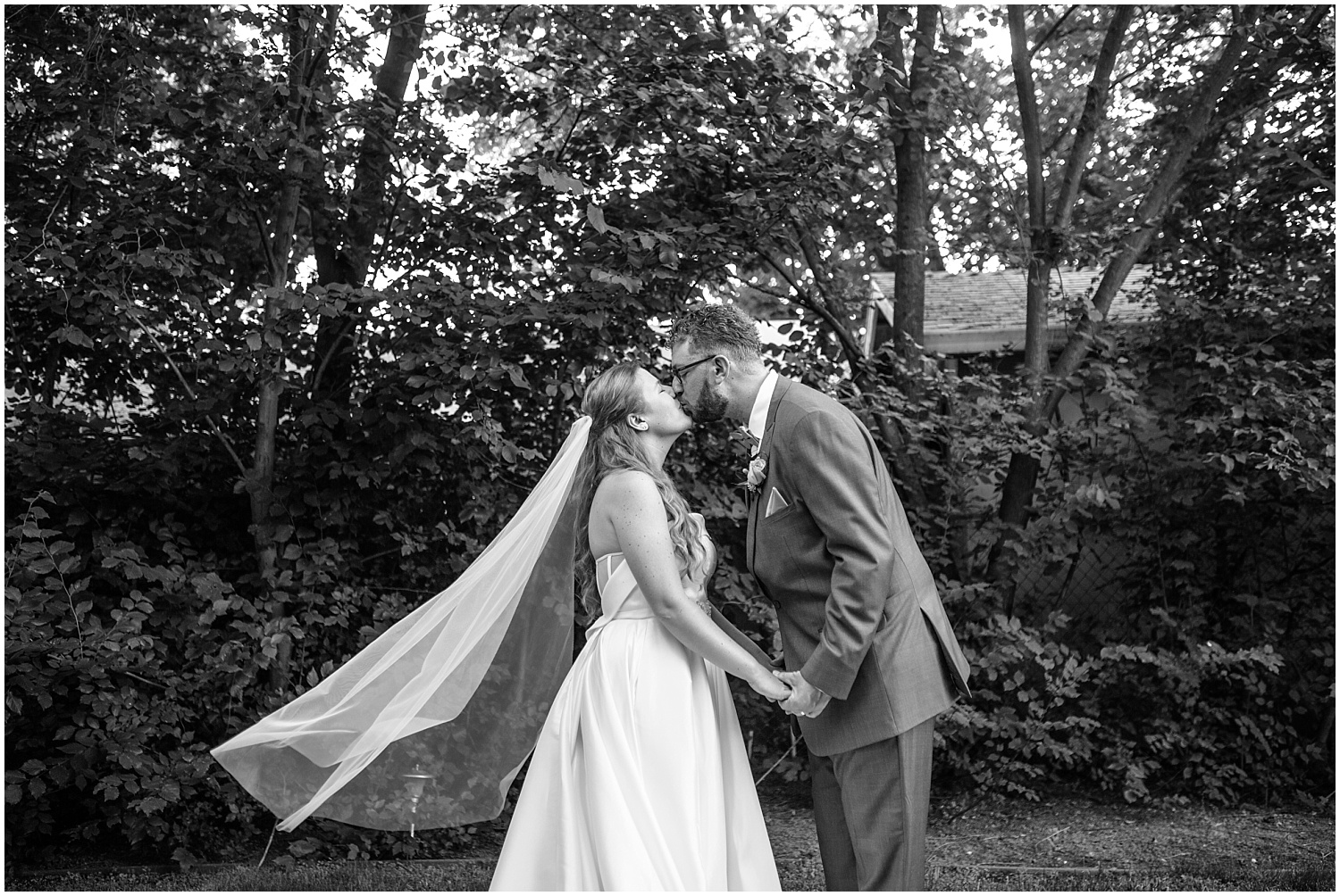 Bride and groom kiss as veil blows in the wind