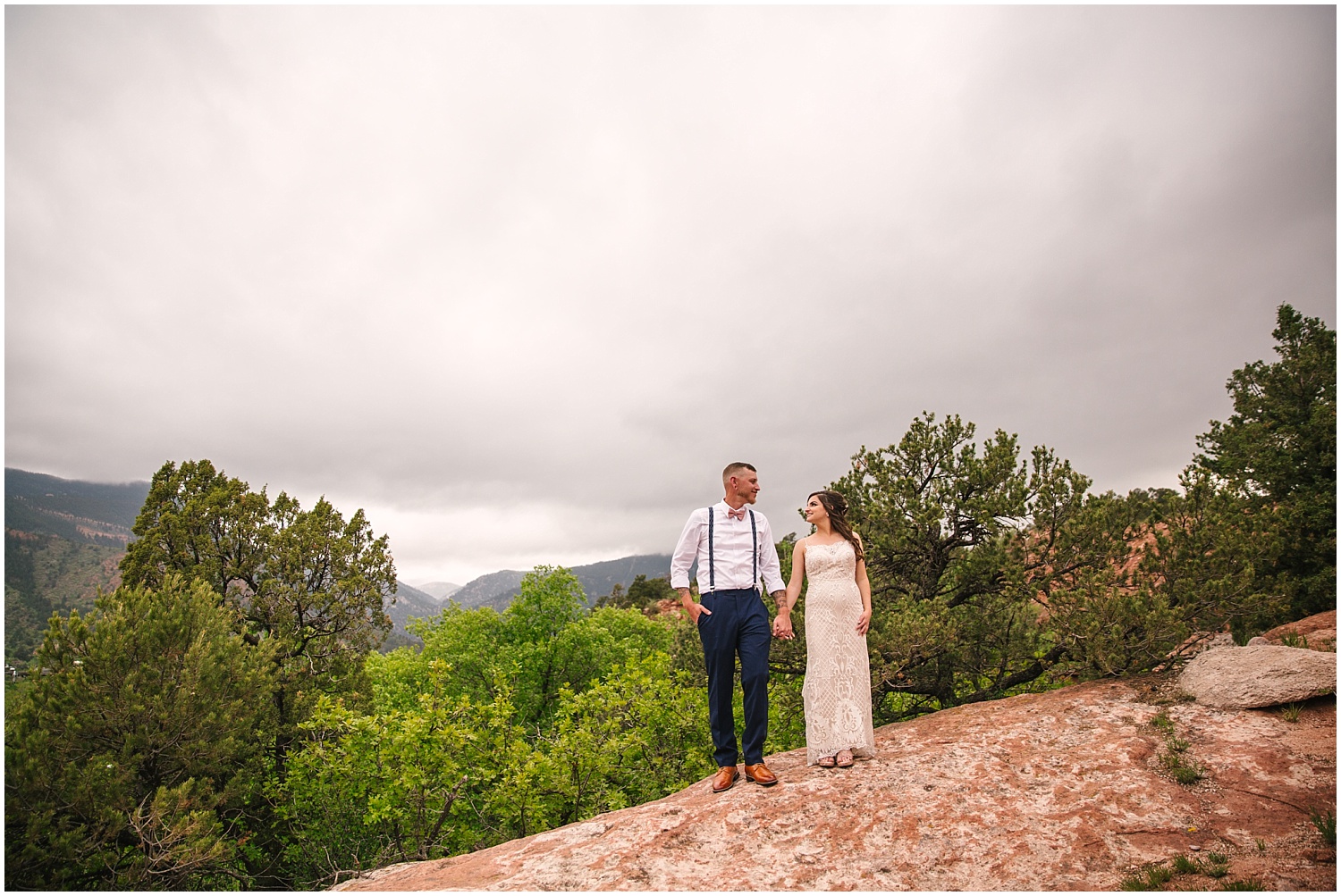 Bride and groom stand on red rocks during thunderstorm over mountains in Manitou Springs Colorado