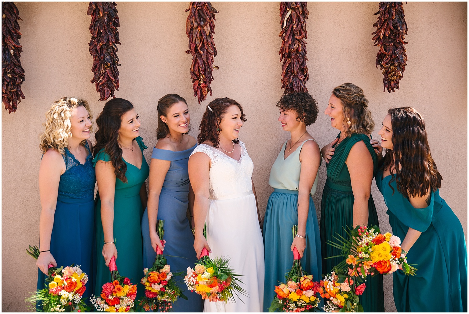 Bridesmaids in mismatched turquoise dresses stand under chile ristras with perfect Santa Fe wedding style