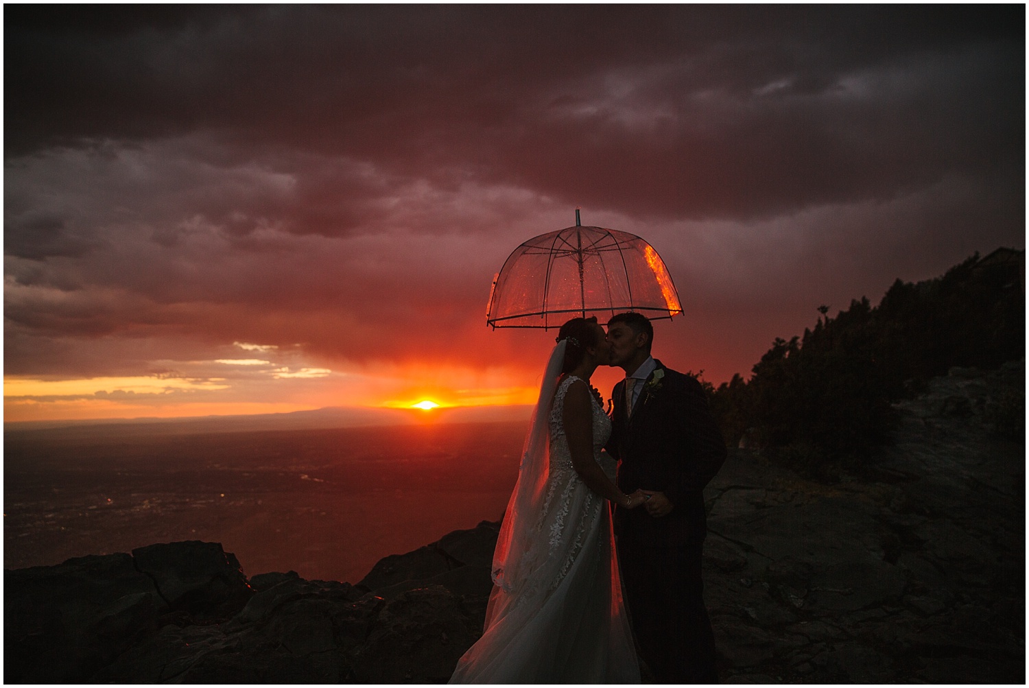 Bride and groom under an umbrella during summer storm at Sandia Crest overlooking Albuquerque