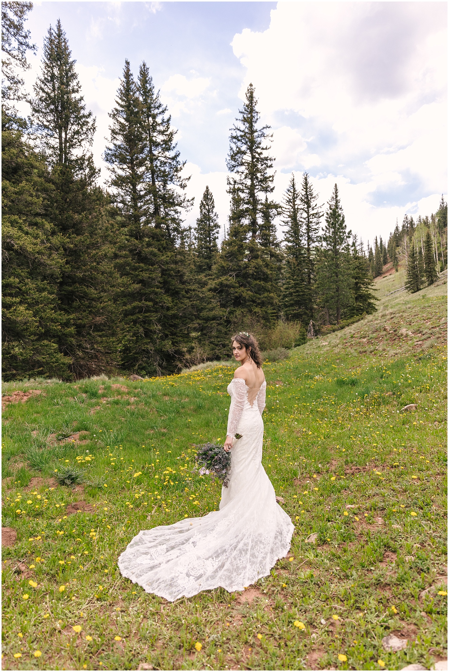 Bride in a long train stands in a field with wildflowers near Telluride Colorado