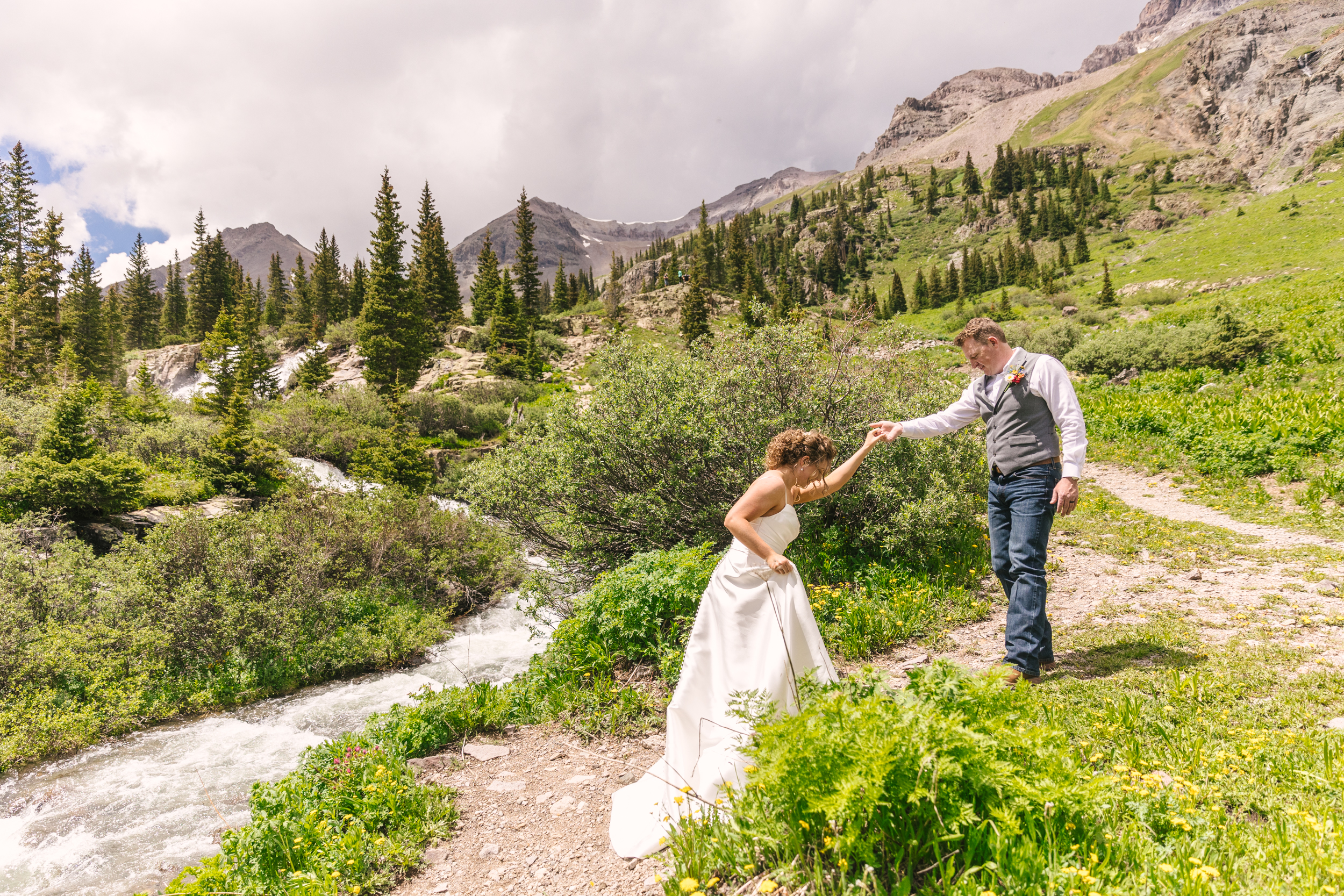 groom assisting bride up a hill in Colorado adventure elopement