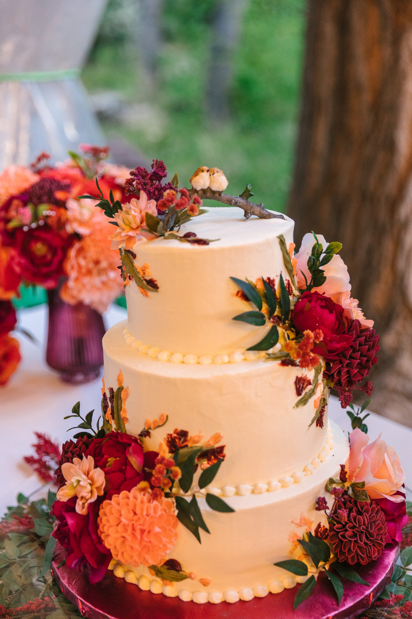 wedding cake with bright florals and pair of birds on top