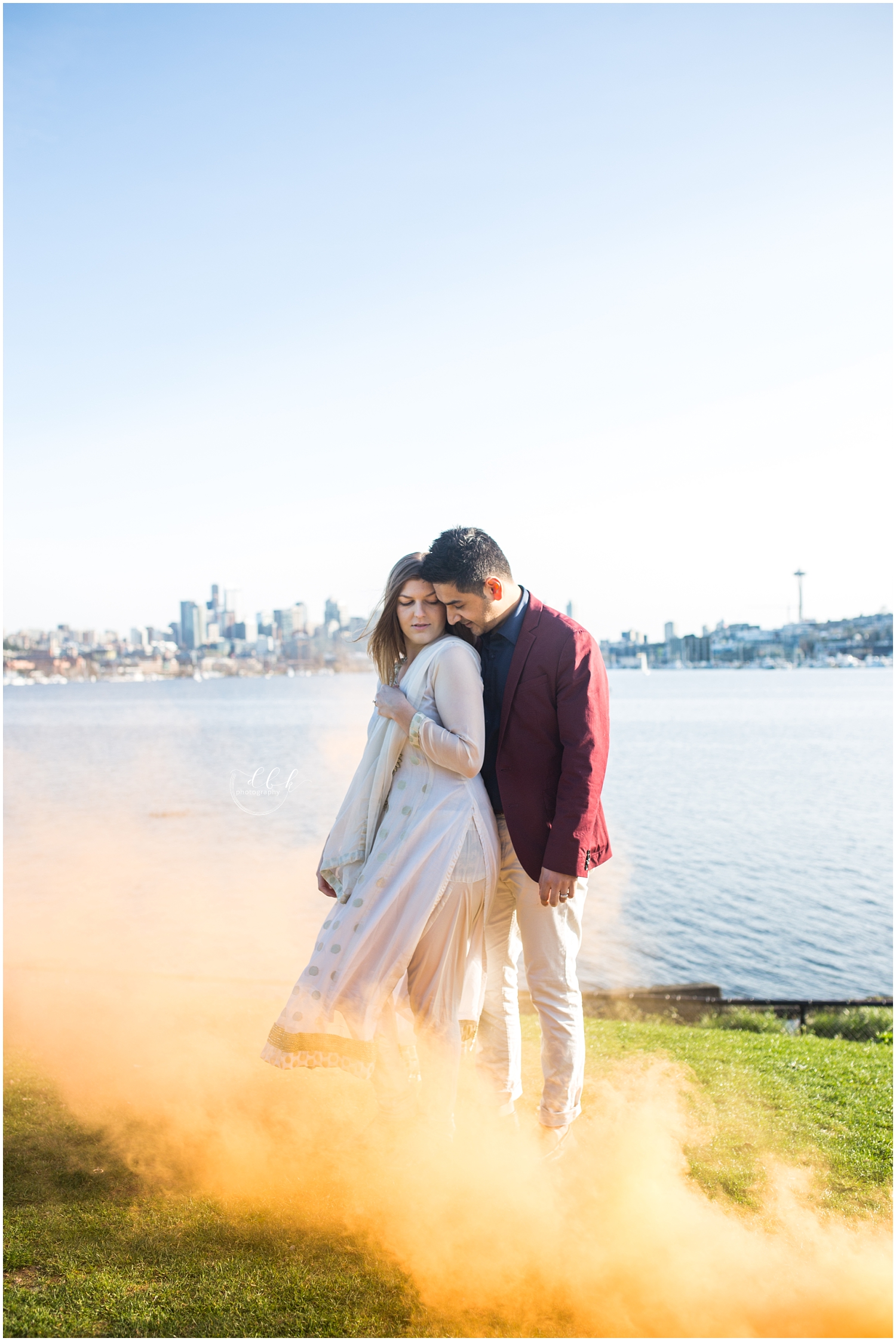 orange colored smoke bomb blowing around couple embracing in front of Seattle skyline at Gas Works Park