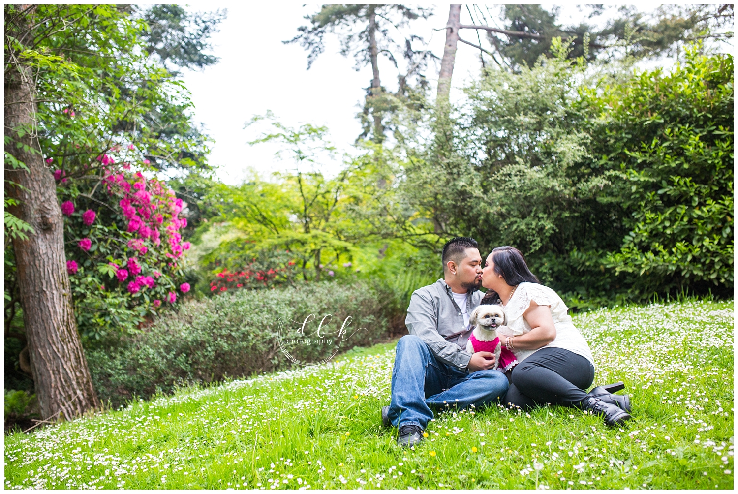 wide shot of couple sitting in grass with their puppy for spring engagement portraits at Kubota Garden
