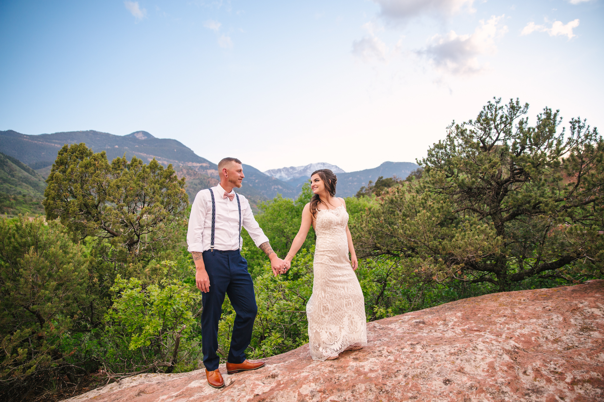 Bride and groom walking along red rocks overlooking Pikes Peak in Manitou Springs