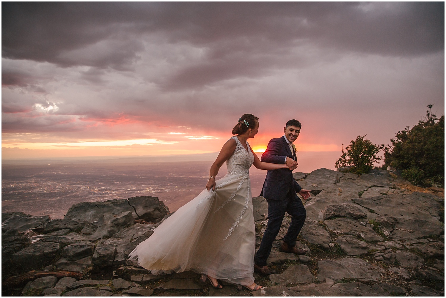 Groom leads bride up the rocks at Sandia Crest as the sun sets behind