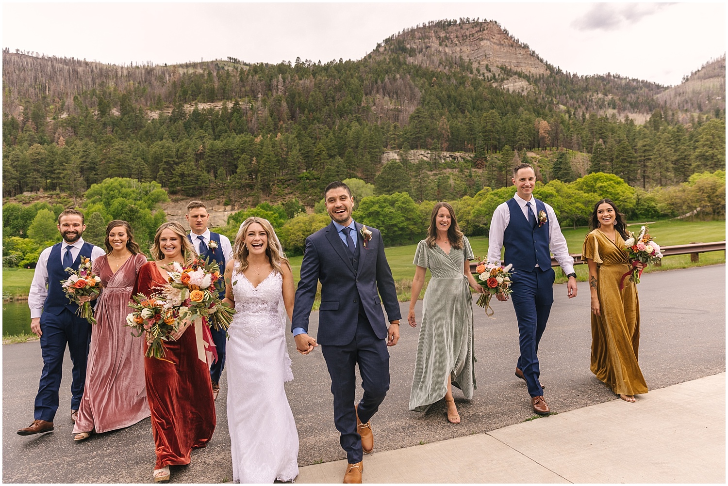 Mismatched wedding party walking across the road surrounded by mountains at Glacier Club wedding in Durango Colorado